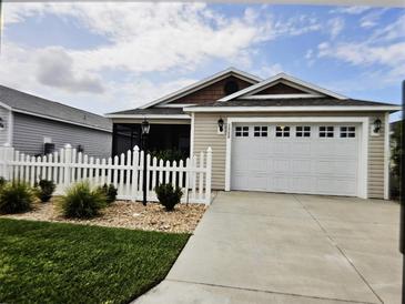 Charming single-story home featuring a well-maintained lawn, white picket fence, and an attached two-car garage at 1964 Rhett Rd, The Villages, FL 32163