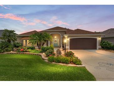Charming single-story home with lush landscaping, a brown two-car garage, and a bright blue front door at 219 Carrera Dr, The Villages, FL 32159