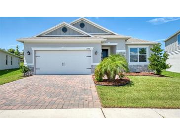 Charming single-story home with a brick driveway, two-car garage, and well-manicured lawn under a blue sky at 1696 Wilson Prairie Cir, Groveland, FL 34736