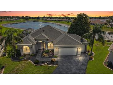 Beautifully landscaped home with a grey roof and a stunning lake view at sunset at 1920 Iglesia St, The Villages, FL 32159
