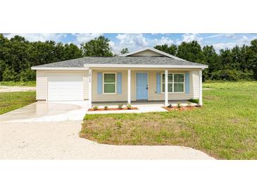 Charming single-story home featuring light siding, blue shutters, a covered front porch, and an attached garage at 10128 County Road 229, Oxford, FL 34484