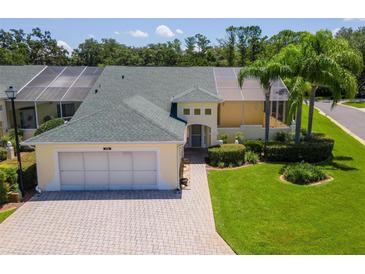 Well-maintained home featuring lush landscaping, palm trees, brick driveway, and a screened-in porch perfect for relaxation at 425 Glen Arbor Ln, Leesburg, FL 34748