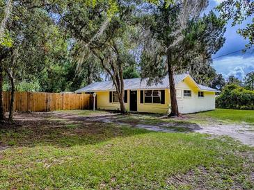 Charming yellow single-story home with a well-maintained lawn, surrounded by mature trees and a wooden fence at 6731 Lake Griffin Rd, Lady Lake, FL 32159