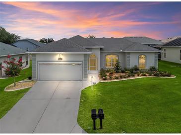 Charming home showcasing manicured landscaping and an attached two-car garage, bathed in warm sunset hues at 16863 Se 110Th Court Rd, Summerfield, FL 34491