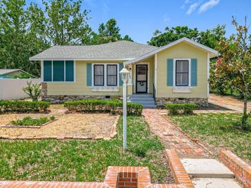 Charming yellow home with blue shutters, complemented by a brick walkway and lush landscaping at 1109 Edmonds St, Leesburg, FL 34748