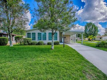 Well-maintained home featuring a spacious front yard, covered carport, and lush landscaping under a bright, partly cloudy sky at 601 Jason Dr, The Villages, FL 32159