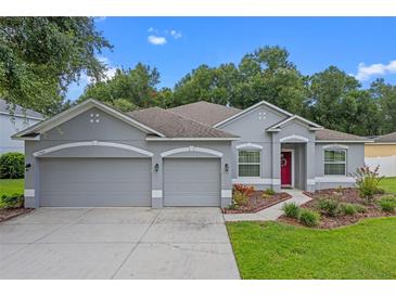 Beautiful single-story home featuring a three-car garage, landscaped yard, and a charming red front door at 1702 Hoofprint Ct, Fruitland Park, FL 34731