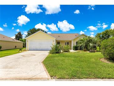 Charming home with a well-manicured lawn, mature trees, and a long driveway leading to a two-car garage at 2450 Merida Cir, The Villages, FL 32162