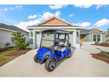 View of the home's exterior featuring a Yamaha golf cart parked in the driveway and a two car garage at 2055 Merideth Ter, The Villages, FL 34762