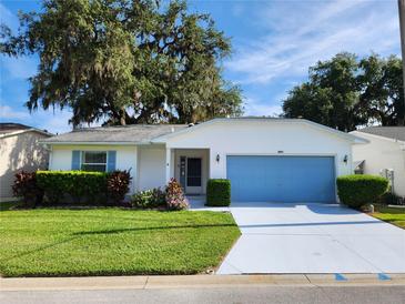 Charming single-story home with a well-manicured lawn, blue garage door, and lush landscaping at 651 Timbercrest Dr, Leesburg, FL 34748