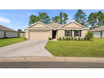 Tan house with a two-car garage and well-manicured lawn at 141 Hickory Course Cir, Ocala, FL 34472