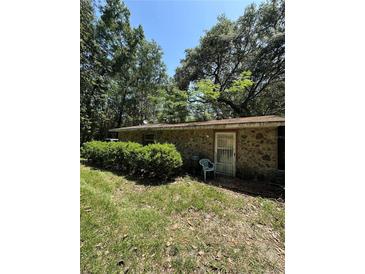 Exterior view of a stone sided home with lush, mature trees, greenery and overgrown lawn at 15750 Ne 150Th Ter, Fort Mc Coy, FL 32134