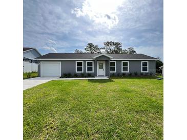 Charming single-story home featuring a manicured lawn, attached garage, and gray exterior at 15433 Sw 47Th Avenue Rd, Ocala, FL 34473
