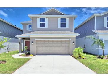 Two-story home with a two-car garage, tan siding, white shutters, and well manicured lawn and landscaping at 1417 Leamington Ln, Winter Haven, FL 33884