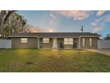 Tan brick ranch house with rocking chairs on the front porch, a well-maintained lawn, and a white fence at 616 W Remington Rd, Lakeland, FL 33813