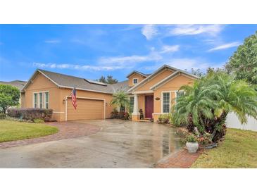 Tan house with a two-car garage, lush landscaping, and a brick paver driveway at 178 Magneta Loop, Auburndale, FL 33823