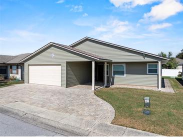 Single-story home features a two car garage, stone paver driveway, manicured lawn, and neutral-colored exterior at 1957 Prairie Dunes N Cir, Lakeland, FL 33810