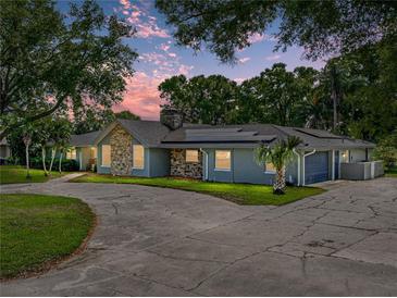 Charming single-story home featuring a stone facade, solar panels, mature trees, and a spacious driveway at 121 Greenfield Rd, Winter Haven, FL 33884