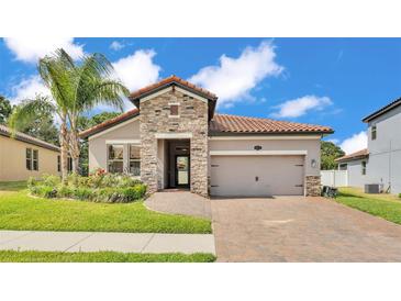 Charming home featuring a stone facade, clay tile roof, and a well-manicured lawn at 2277 Bella Luna Cir, Lakeland, FL 33810