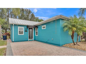 Charming blue home features a brick driveway and a metal roof surrounded by palm trees at 3243 Red Tail Hawk Dr, Polk City, FL 33868
