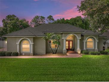 Home's exterior at dusk with manicured lawn, palm trees, and inviting arched entry at 148 Melissa Trl, Auburndale, FL 33823