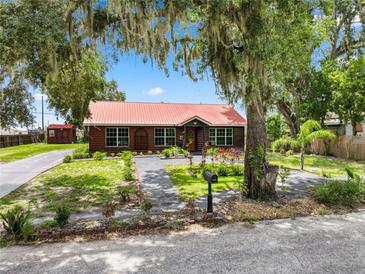 Charming log home with a red metal roof, mature trees, and landscaped yard at 330 Diesel Rd, Mulberry, FL 33860