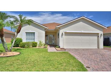 Charming single-story home featuring a manicured lawn, palm trees, and a brick driveway leading to a two-car garage at 4188 Muirfield Loop, Lake Wales, FL 33859