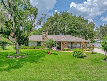 Charming stone home with a well-manicured front lawn and mature trees under a beautiful sky at 1308 Timberidge N Loop, Lakeland, FL 33809