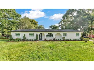 Charming single-story home featuring a white facade, arched entryway, and lush green lawn with mature trees at 3235 Sandpiper Ln, Mulberry, FL 33860