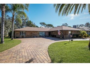 Brick ranch house with paver driveway, mature landscaping, and American flag at 803 Silk Oak Ct, New Smyrna Beach, FL 32168