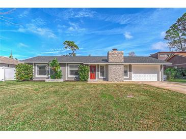 Gray house with red door, stone chimney, and attached garage. Lush lawn at 2507 Milton Ave, New Smyrna Beach, FL 32168