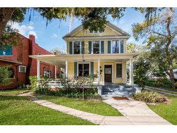 Two-story yellow house with a wraparound porch, landscaping, and mature trees at 608 Magnolia St, New Smyrna Beach, FL 32168