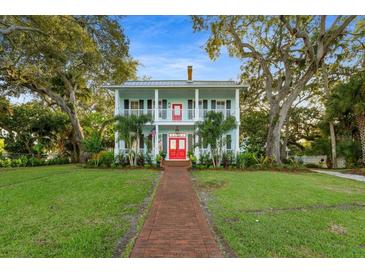 Two-story light blue house with red door, brick pathway, and lush landscaping at 504 N Riverside Dr, New Smyrna Beach, FL 32168