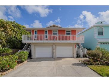 Two-story home showcasing a salmon exterior, two-car garage and white railing under a blue sky with white clouds at 6443 Engram Rd, New Smyrna Beach, FL 32169