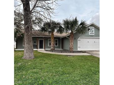 Charming single-story home features green siding, a two-car garage, and well-maintained landscaping with palm trees at 956 Tall Pine Dr, Port Orange, FL 32127
