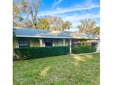 Charming single-story home featuring a lush green lawn, decorative porch columns, and vibrant flowering shrubs at 485 Merrimac Dr, Port Orange, FL 32127