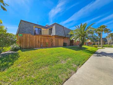 Charming two-story townhouse with a wood fence, lush lawn, and a view of palm trees against a clear blue sky at 61 Cedar Dunes Dr, New Smyrna Beach, FL 32169