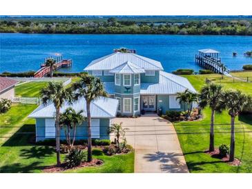 Waterfront home featuring lush landscaping, an eye-catching metal roof, and a large driveway leading to the entrance at 2019 S Riverside, Edgewater, FL 32141