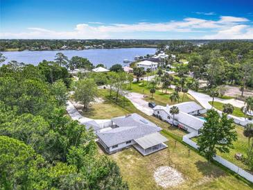 Expansive aerial view of a single story home next to a lake surrounded by lush greenery and an inviting neighborhood at 1812 Bayview Dr, New Smyrna Beach, FL 32168