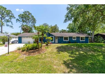 Charming blue home features a manicured lawn, tropical landscaping, and a welcoming entrance at 35 Knollwood Estates Dr, Ormond Beach, FL 32174