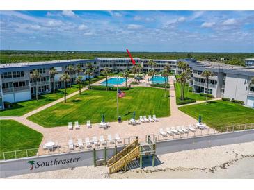 Beautiful aerial view of the condo complex with lush green lawn, two pools, and the beach in the background at 4841 Saxon Dr # C201, New Smyrna Beach, FL 32169