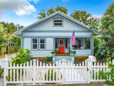 Charming light blue cottage featuring a white picket fence, orange door, and well-maintained landscaping at 216 Murray St, New Smyrna Beach, FL 32168