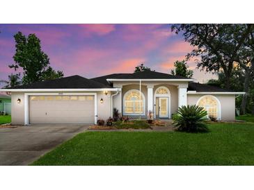 Charming home featuring a two-car garage, arched windows, and a well-maintained lawn at 5935 Shady Creek Ln, Port Orange, FL 32128