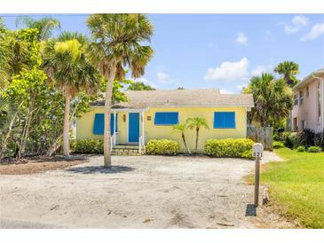 Charming yellow bungalow with blue shutters, palm trees, and a sandy front yard, offering a classic beach vibe at 821 Ocean Ave, New Smyrna Beach, FL 32169