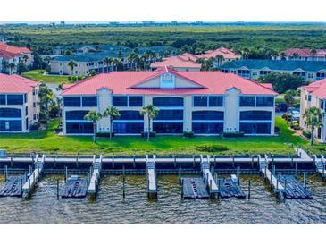 Waterfront condo featuring a red roof, a boat dock, screened-in patios, and lush grassy areas at 454 Bouchelle Dr # 202, New Smyrna Beach, FL 32169