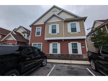 Two-story townhome with tan and red siding, white trim, and a spacious front yard at 7532 Sunville Ave, Kissimmee, FL 34747