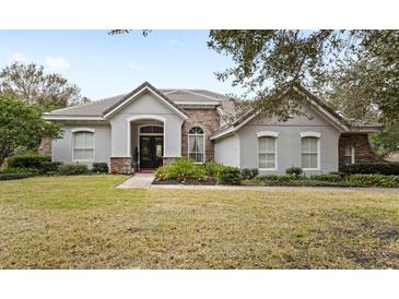 One-story house with gray stucco, stone accents, and a tile roof, showcasing a manicured lawn at 25515 Hawks Run Ln, Sorrento, FL 32776