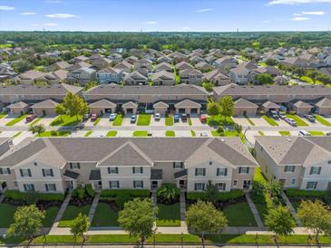 Expansive aerial view of a neighborhood showcasing rows of townhomes, landscaped streets, and verdant greenery, under a bright blue sky at 1625 Reflection Cv, Saint Cloud, FL 34771
