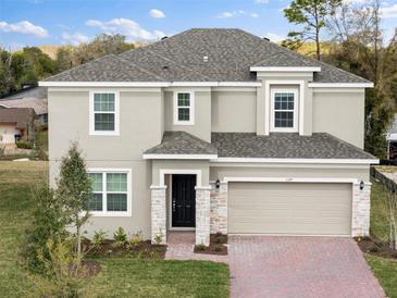 Two-story home with a tan exterior, a two-car garage, stone accents, and a brick driveway at 1197 Happy Forest Loop, Deland, FL 32720