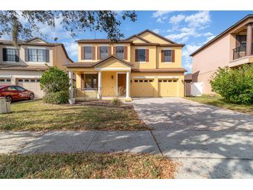 Two-story house with a yellow facade, brick driveway, and landscaping at 10064 Silver Laurel Way, Orlando, FL 32832